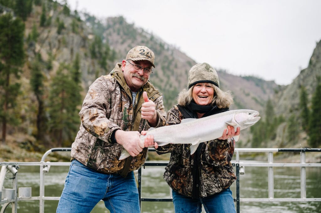A man and a woman hold a silver colored steelhead during an Idaho steelhead fishing trip on the Salmon River.
