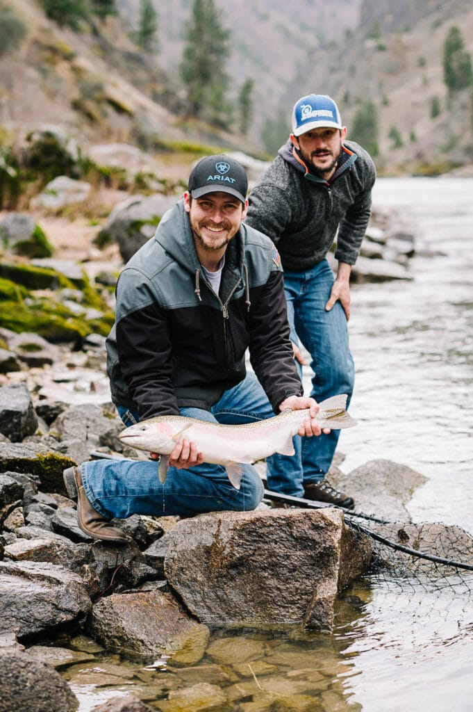 A smiling fisherman holds a steelhead fish on the bank of the Salmon River. Whitewater Expeditions offers Riggins steelhead fishing trips on the Salmon River.