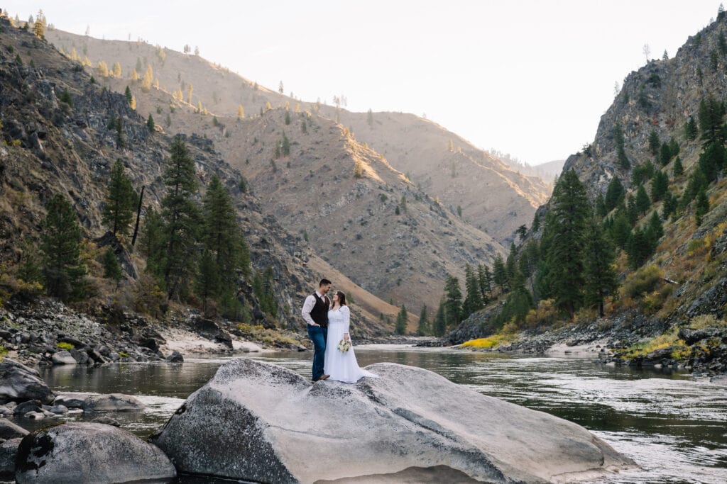 A Bride and groom stand on a rock in the middle of the Salmon River at sunrise. This couple eloped on the Salmon River in with Whitewater Expeditions.